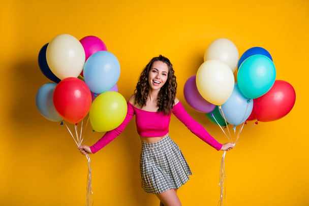 Portrait photo of positive smiling girl wearing casual off-top checkered skirt holding air balloons preparing for party isolated on vivid yellow color background - Φωτογραφία, εικόνα