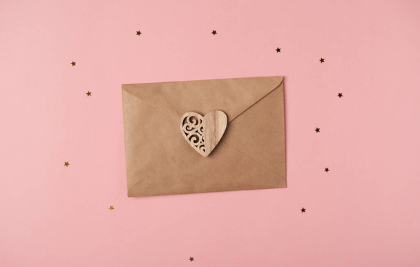 Craft envelope with the wooden heart on the hot pink background. Flat lay, top view. Romantic love letter for Valentine's day concept. - 写真・画像