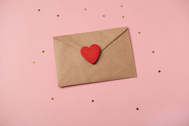Craft envelope with the wooden heart and little golden stars on the rose background. Flat lay, top view. Romantic love letter for Valentine's day concept. - Zdjęcie, obraz