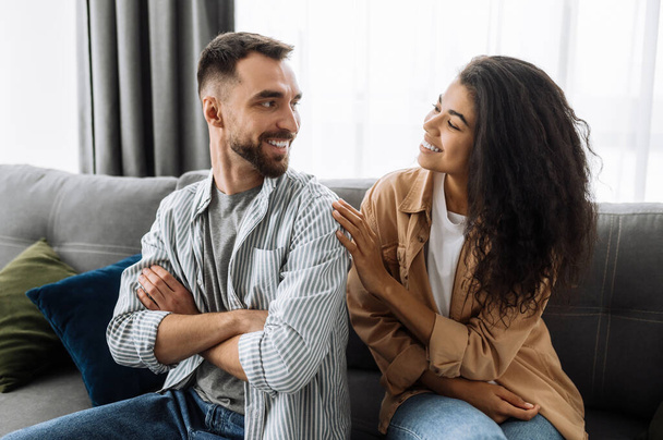 Cheerful married couple chilling at home, sitting on the sofa. Caucasian husband looks with love at her beautiful african american wife, weekend together - Fotoğraf, Görsel