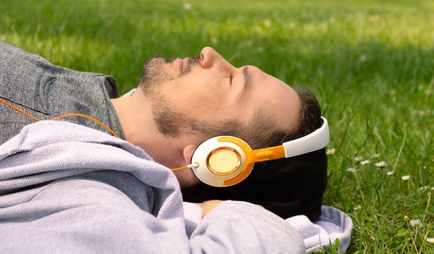 ヘッドフォンで音楽を楽しみ、自然の中で芝生の上でリラックスした無料の男.  - 写真・画像