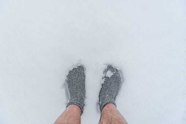 Vista personale con i piedi uomo vestito solo in calzini in piedi sulla neve bianca pulita. Sopra la vista con le gambe dell'uomo nella neve profonda - Foto, immagini