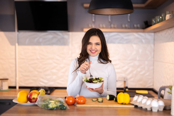 Красивая улыбающаяся молодая женщина готовит здоровую пищу с большим количеством фруктов и овощей на домашней кухне - Фото, изображение