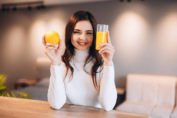 Beautiful young woman drinking fresh orange juice in kitchen. Healthy diet. - Photo, Image