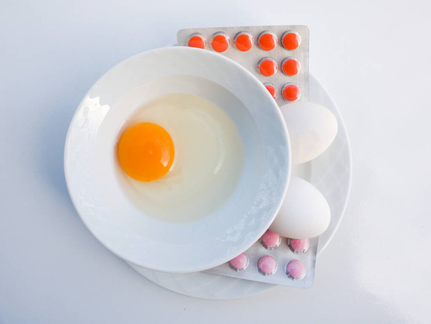 Eigeel in een kom. Twee eieren in een kom en vitaminepillen. Geneeskunde of een gezond dieet. Dierlijk voedsel en vitaminen. Vitamine b. - Foto, afbeelding