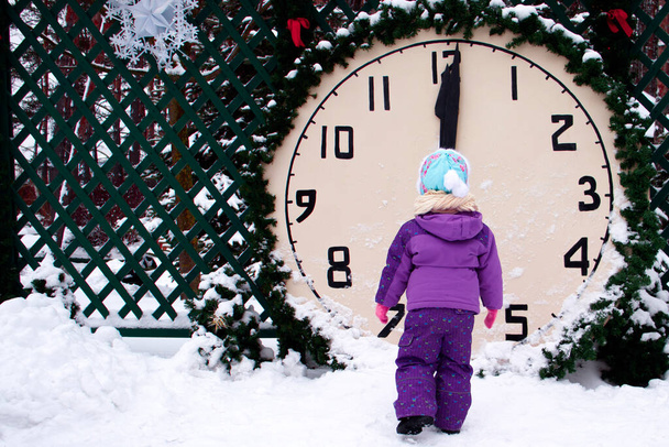 The child looks at the clock against the background of winter, there is snow around, time is 12. Christmas fairy tale concept. - Foto, imagen