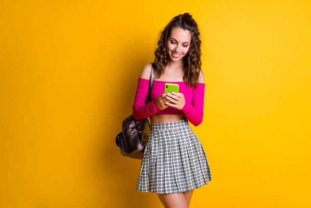 Photo of pretty charming lady hold telephone chatting email toothy white smile wear rucksack pink top uncovered shoulders mini skirt isolated yellow color background - Φωτογραφία, εικόνα