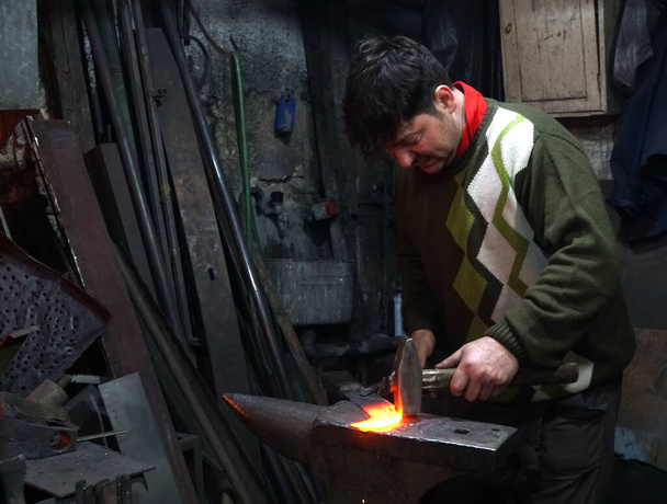 Smid met hamer die werkt aan een verwarmde ijzeren sikkel in de werkplaats - Foto, afbeelding