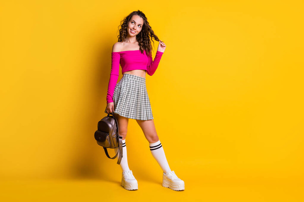 Full length photo of lady curly hairdo look empty space hold bag play curl wear pink top unclothed shoulders mini skirt white stockings sneakers isolated yellow color background - 写真・画像