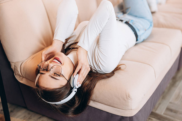 Nice girl wearing headphones is listening to music at home laying on sofa. Photo about young lady is having relax at home. - Foto, imagen
