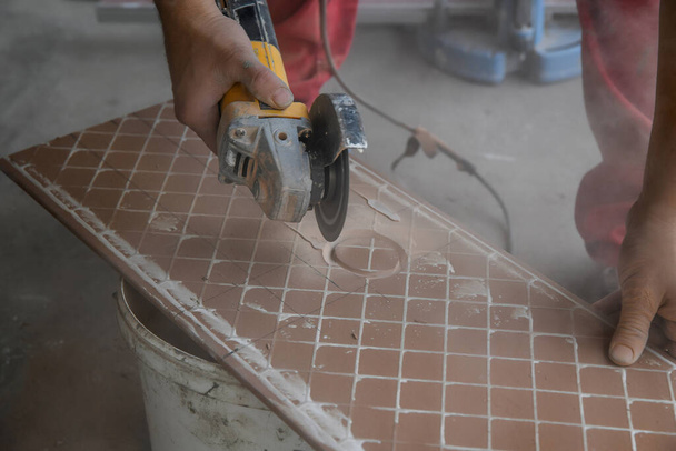 Het snijden van keramische tegels. Een arbeider plaatst een grote keramische tegel in een snijmachine. Opening van een gat in de tegel - Foto, afbeelding