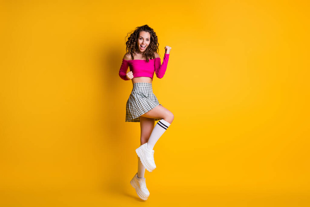 Full body size photo of lovely cute lady wavy hairdo raise arms fists open mouth jump wear pink cropped top uncovered shoulders mini skirt white sneakers isolated yellow color background - Foto, Imagen
