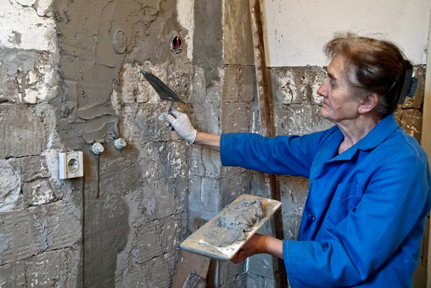 Женщина-рабочий оштукатуривает бетон у стены дома - Фото, изображение