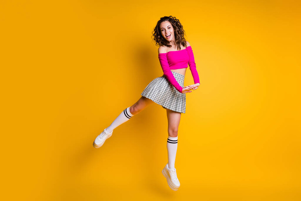 Photo portrait of girl happily jumping up holding hands together wearing pink crop-top plaid skirt knee-high socks white trainers isolated on vivid yellow colored background - Valokuva, kuva