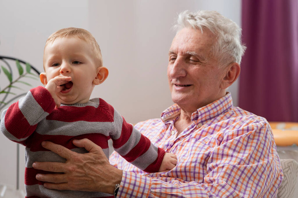 Portré játékos kisfiú és mosolygós nagyapa élvezik szórakozni együtt otthon   - Fotó, kép