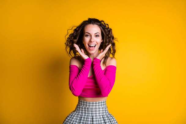 Photo portrait of excited woman holding hands near face smiling wearing pink crop-top checkered skirt isolated on vivid yellow colored background - Foto, imagen