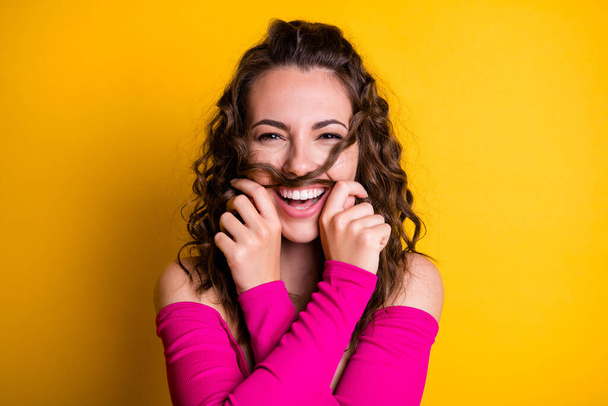 Photo portrait of silly brunette girl making hair mustache laughing holding with two hands wearing fuchsia crop-top isolated on vivid yellow colored background - Valokuva, kuva