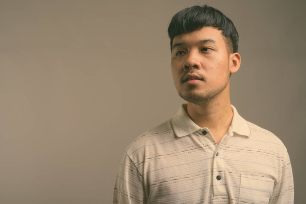 Portrait of young Asian man against gray background - Φωτογραφία, εικόνα