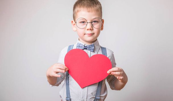 Öt éves, mosolygós fiú, piros szívvel, a szeretet, a család, a remény szimbólumával. Háttér kártyák Valentin-napon vagy társadalmi plakátok a család és a gyermekek megőrzéséről. - Fotó, kép