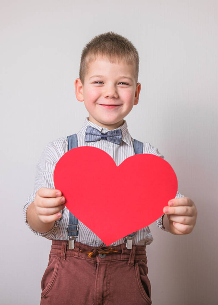 Öt éves, mosolygós fiú, piros szívvel, a szeretet, a család, a remény szimbólumával. Háttér kártyák Valentin-napon vagy társadalmi plakátok a család és a gyermekek megőrzéséről. - Fotó, kép