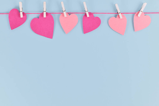 シンプルなバレンタインデーの背景とピンクの紙の心は空のコピースペースとペグでラインからぶら下がっています  - 写真・画像