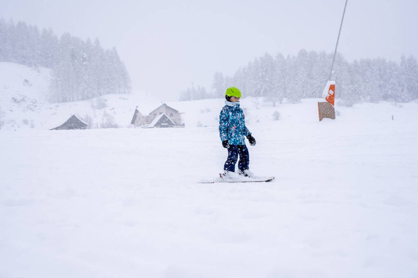 Downhill skiing during a heavy snowfall. Child skiing in mountains. Active kid with safety helmet and goggles. Ski race for young children. Kids ski lesson in alpine school. Blurred focus background - Photo, Image