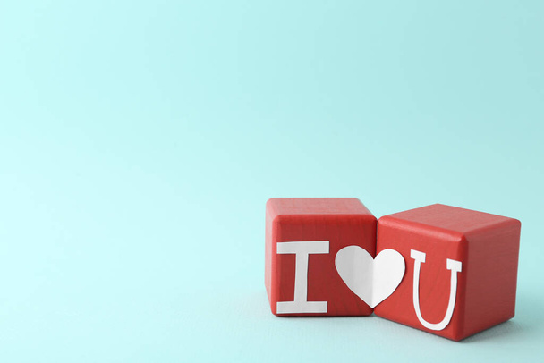 Phrase I Love You made of paper letters and heart connecting two red cubes on light blue background - Zdjęcie, obraz
