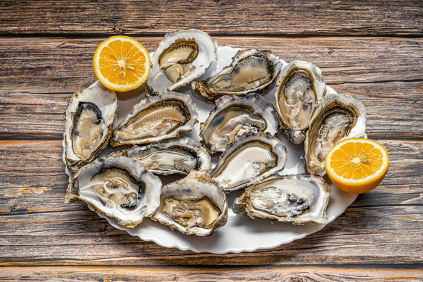 Vers geopende oesters in een witte plaat met citroen op donkere houten textuur achtergrond, bovenaanzicht - Foto, afbeelding