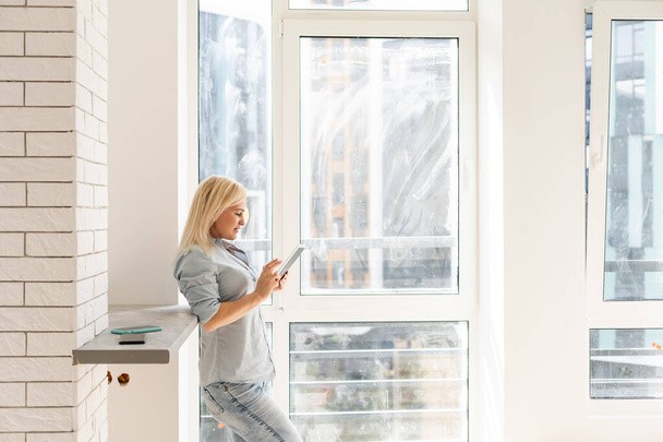 Frau mit Tablet auf der Suche nach Reinigung, um schmutzige Fenster zu waschen - Foto, Bild