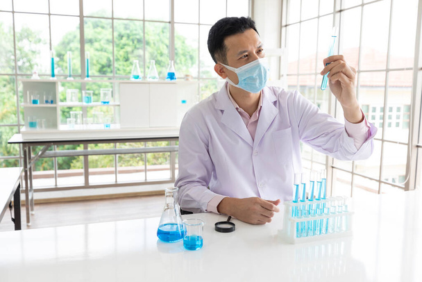 scientifique homme portant un masque facial médical faisant ou testant une expérience chimique en laboratoire - Photo, image