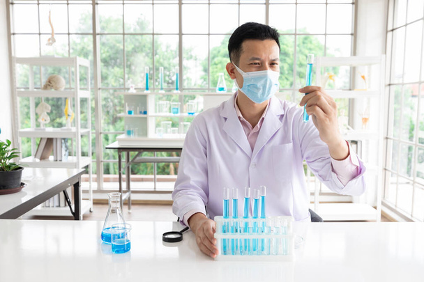 scientifique homme portant un masque facial médical faisant ou testant une expérience chimique en laboratoire - Photo, image