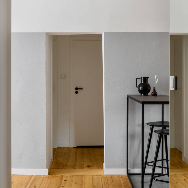 Yksinkertainen huone harmaa ja valkoinen seinät, mänty puu lattialla ja tyylikäs pitkä musta pöytä, jossa kaksi, musta baari ulosteet - Valokuva, kuva