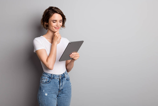 Photo of attractive young girl hold pc tablet read browse news information hand touch chin isolated over grey color background - Foto, Imagen