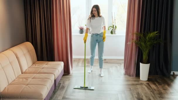 Een jonge vrouw maakt thuis schoon. Brunette model wast de vloer in de woonkamer. - Video