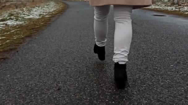 Задняя сторона девушки или женщины, идущей по улице в туфлях на высоких каблуках в зимней куртке, прыгает и делает смешной трюк с ногой. Наслаждаясь зимой во время прогулки в одиночку в сельской местности - Кадры, видео