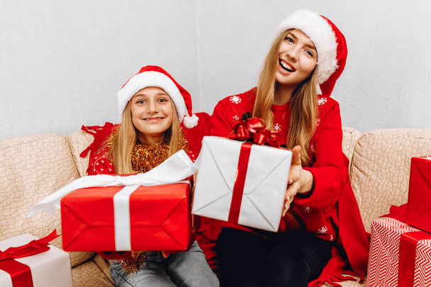 Happy family, beautiful mother and her little daughter in Santa Claus hats, are sitting at home on the couch with Christmas gifts, loving family with gifts, Merry Christmas and Happy New Year - Φωτογραφία, εικόνα