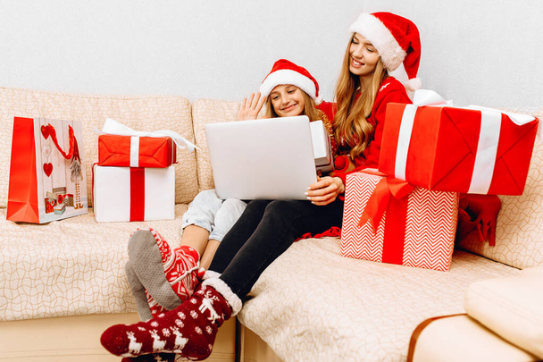 Family with a child, mom and her little girl, making a video call through a laptop, sitting on the couch at home for Christmas - Φωτογραφία, εικόνα