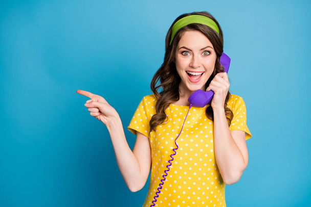 Photo portrait of curly brunette talking on violet telephone pointing finger at copyspace isolated on pastel light blue colored background - Foto, Imagem