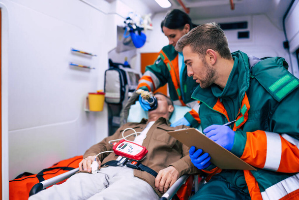 Doctors emergency or paramedics are working with a senior man patient while he lies on a stretcher in an ambulance. - Photo, image