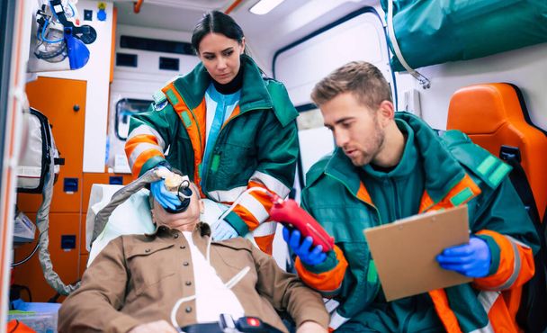 Médicos de emergencia o paramédicos están trabajando con un paciente mayor mientras él se acuesta en una camilla en una ambulancia. - Foto, Imagen