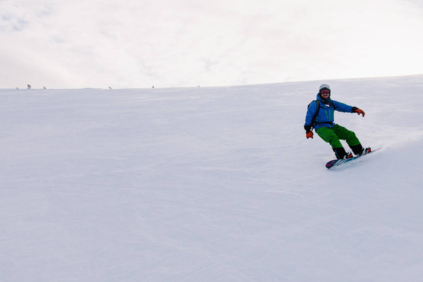 Guy slides on a snowboard down the slope in a bright suit - Foto, afbeelding