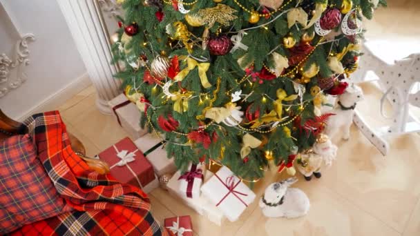 Κάτοψη του πολλά κουτιά δώρων κάτω από διακοσμημένο χριστουγεννιάτικο δέντρο στο σαλόνι στο όμορφο σπίτι. Χειμερινές διακοπές φόντο ή φόντο. - Πλάνα, βίντεο