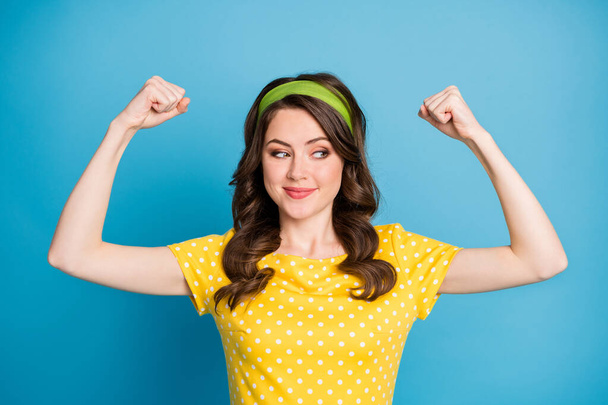 Portrait of positive cheerful girl show her muscles look interested on hand isolated over blue color background - Foto, Imagem