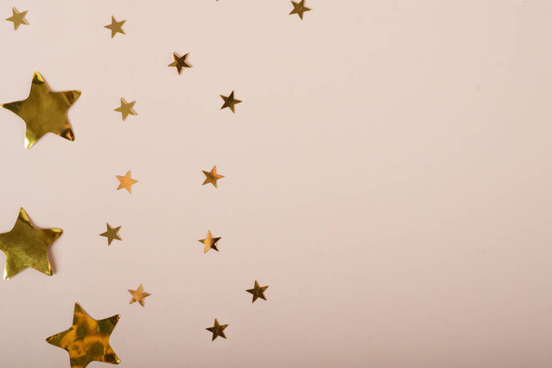 星とベージュの背景。ベージュパステルの背景に金色の星のコフェッティとモミの枝を持つシャンパンボトル。休日、パーティーやお祝いの概念。コピースペースと創造的なフラットレイアウト. - 写真・画像