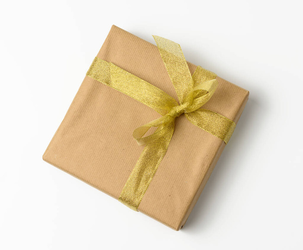 коробка, загорнута в коричневий крафт-папір і зав'язана золотими стрічками, подарунок на білому тлі
 - Фото, зображення