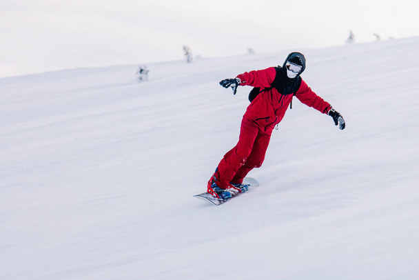 Guy glides down the slope on a snowboard in a red jumpsuit - Zdjęcie, obraz