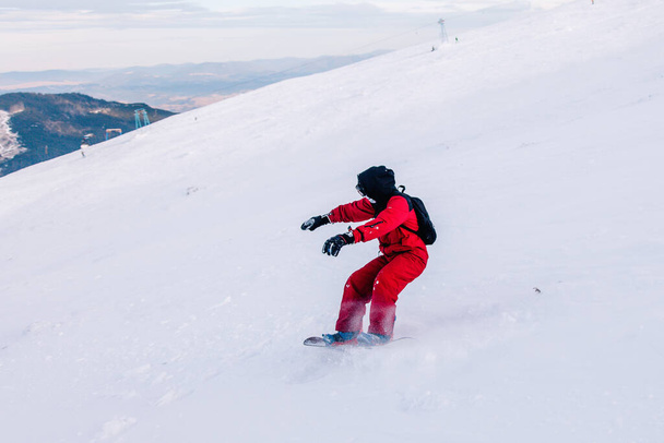 Guy glides down the slope on a snowboard in a red jumpsuit - Foto, Imagen