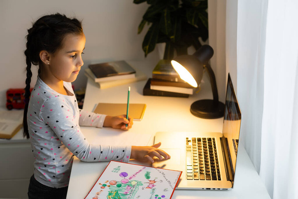 Evde bilgisayarını kullanarak internetten ders çalışan küçük bir kız. - Fotoğraf, Görsel