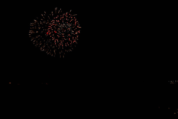 vuurwerk in oranje kleur met rode punten zwarte hemel met kopieerruimte - Foto, afbeelding