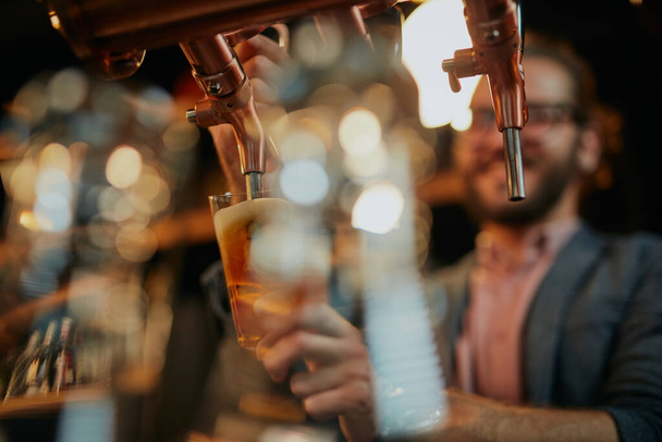 Ένας μπάρμαν ρίχνει μπύρα στο ποτήρι ενώ στέκεται στο μπαρ. - Φωτογραφία, εικόνα